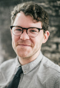 image of Sam Allingham wearing glasses in a grey shirt and black tie