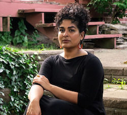 image of Divya Victor in a black dress sitting on brick steps