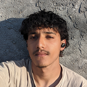 image of Massin standing against a rock wearing earbuds and a tan tee shirt