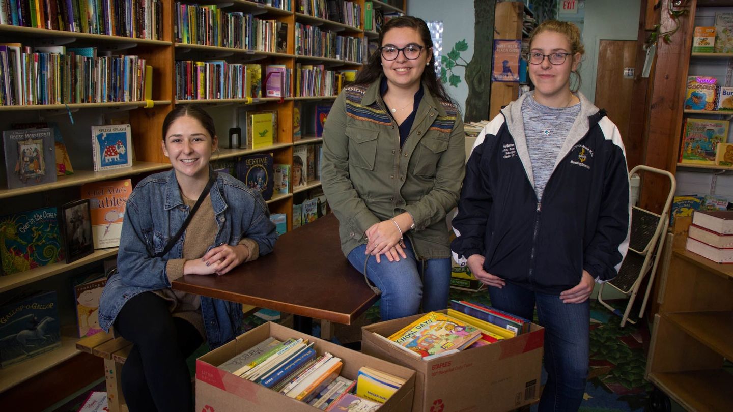 Three College of Liberal Arts student ambassadors pose with boxes of books at Treehouse Books