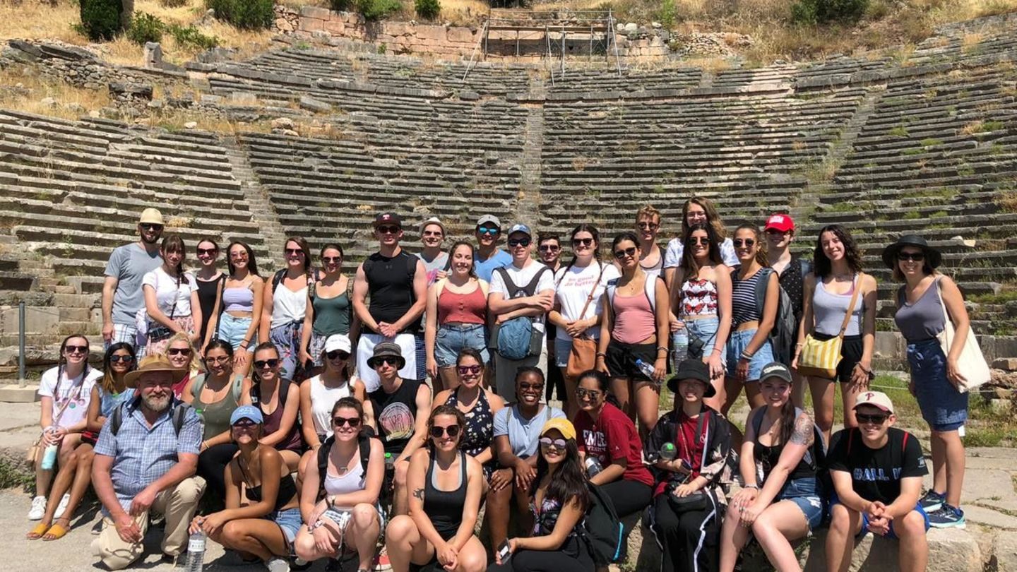 A group of College of Liberal Arts Intellectual Heritage students stand in front of a monument in Athens, Greece, while studying abroad.