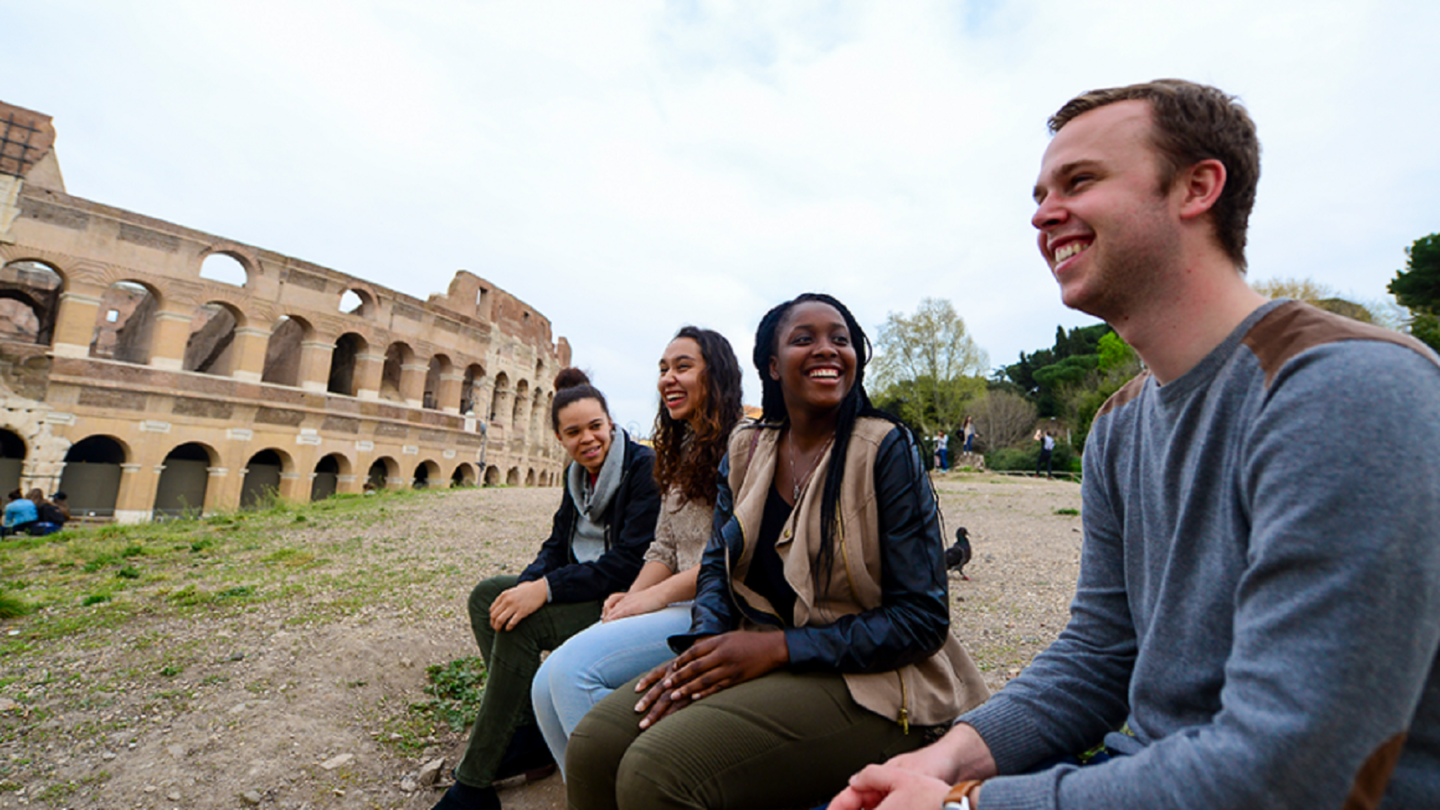 Students sit in front of a colosseum 