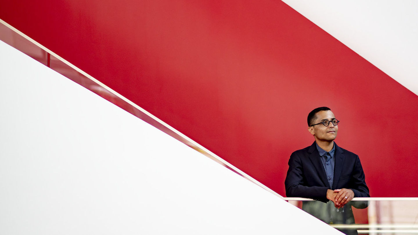 Heath Fogg Davis standing by a staircase with a red background.