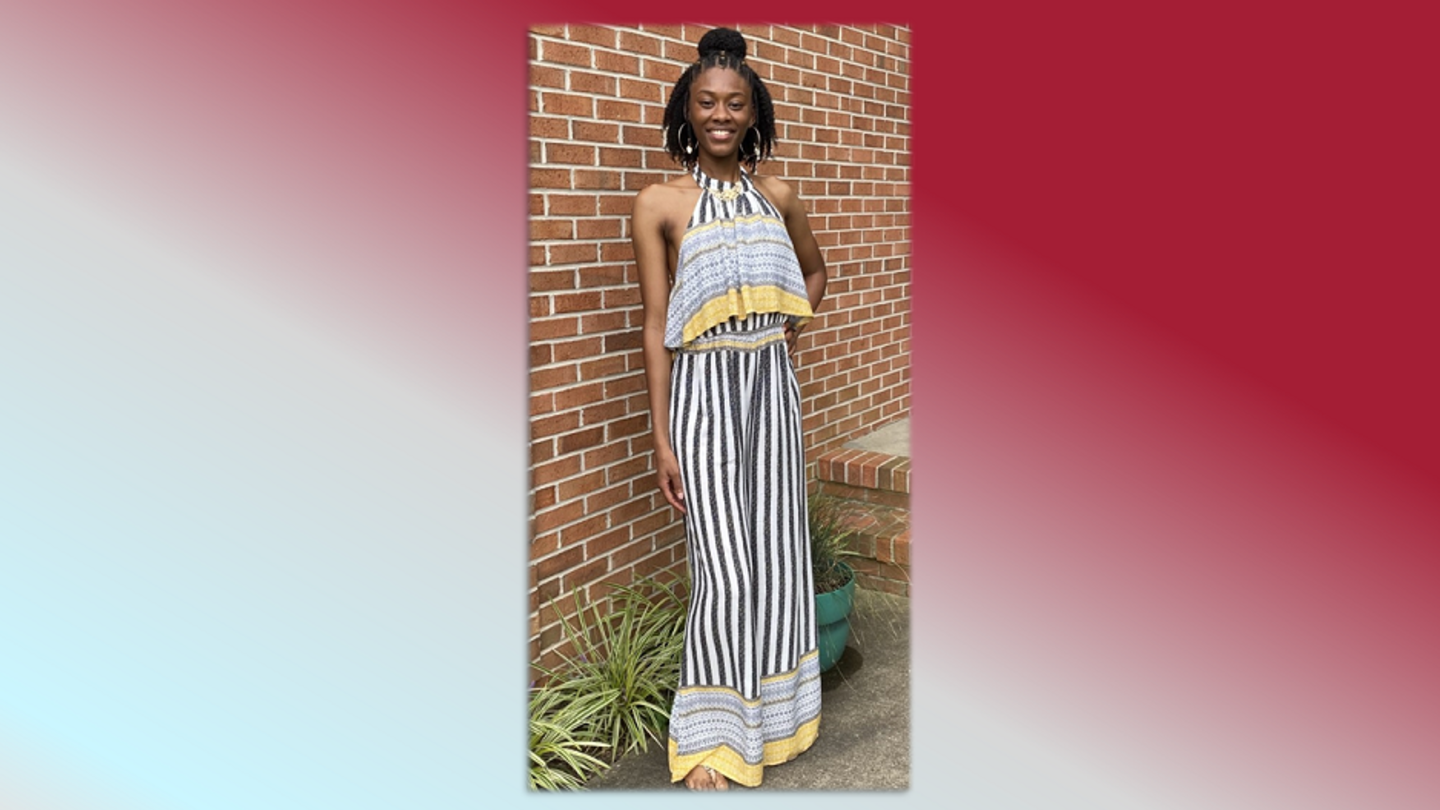 image of Janay Greene in a black and white striped dress standing in front of a brick wall