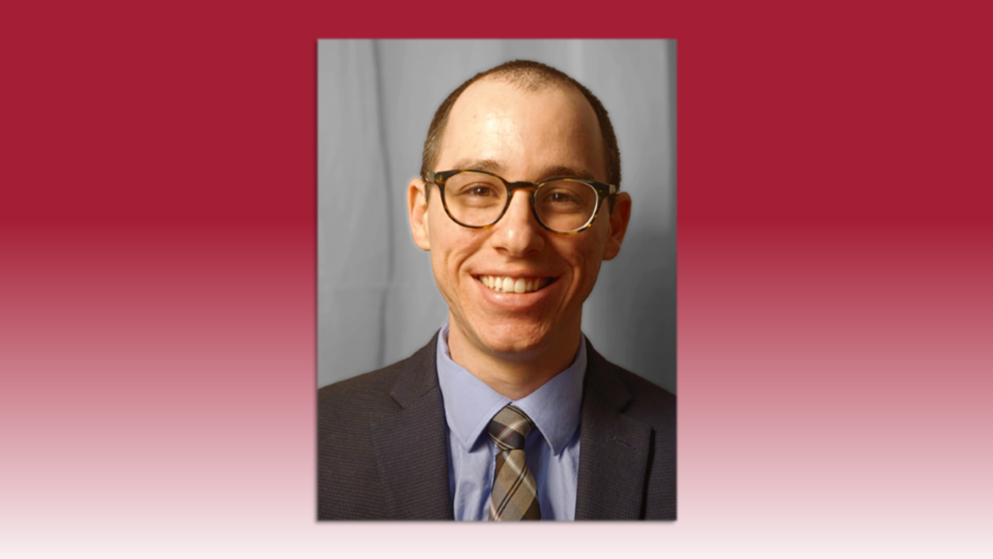 image of Tyler wearing glasses in a grey suit, tie and blue shirt