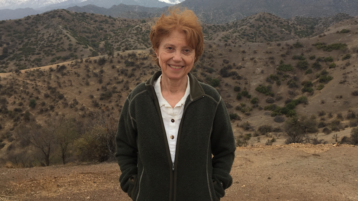 image of Nora standing in the desert wearing a black jacket smiling with the mountains behind her