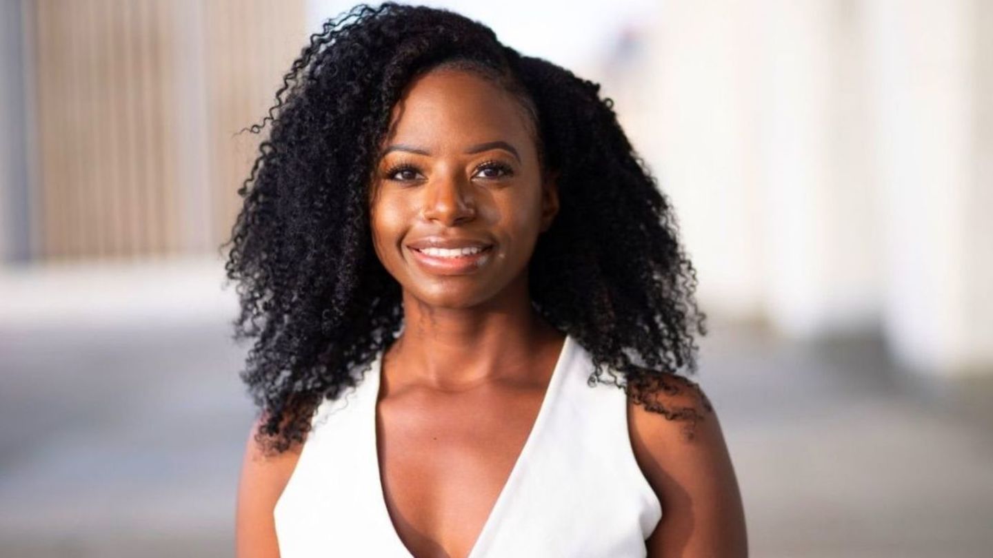 image of Noel smiling at the camera wearing a white sleeveless top