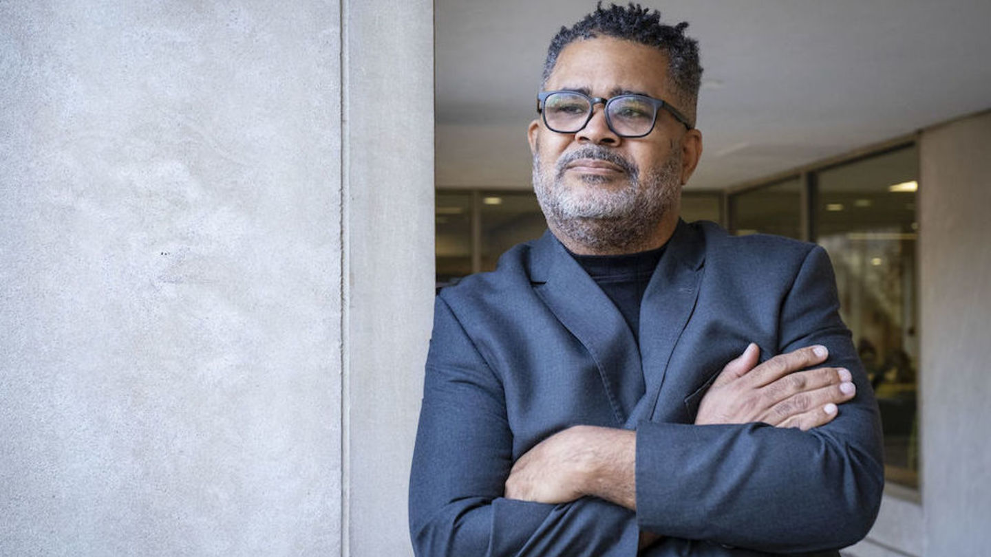 image of Reynaldo wearing glasses looking off into the distance standing with his arms crosssed wearing a blue suit leaning on a column outside of Gladfelter Hall