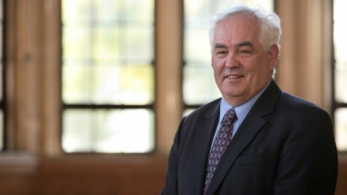 image of Peter wearing a black suit, sitting and smiling at the camera in Mitten Hall